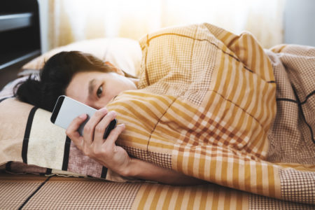 un adolescent utilisant un téléphone intelligent le matin, vérifiant le message après le réveil